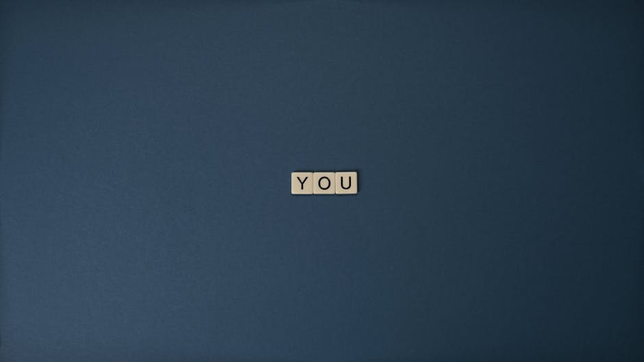 Flat lay of Scrabble letters spelling 'YOU' on a blue background, perfect for conceptual themes.